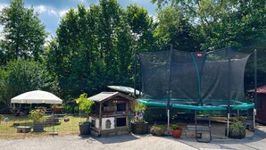 A fenced outdoor area with a wooden playhouse, a trampoline with a safety net, and potted plants. - Simssee Vacation Rental, 45 square meters (Rimsting)