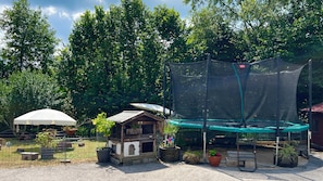 A fenced outdoor area with a wooden playhouse, a trampoline with a safety net, and potted plants. - Simssee Vacation Rental, 45 square meters (Rimsting)