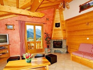 A cozy living room with a fireplace, wooden furniture, and a view of mountains. - Paradis de St.Martin by Interhome (Les Granges)