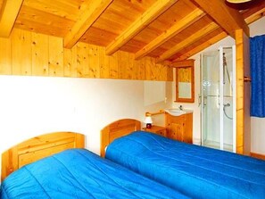 A room with two wooden beds, a bathroom with a glass shower, and a wooden ceiling. - Paradis de St.Martin by Interhome (Les Granges)