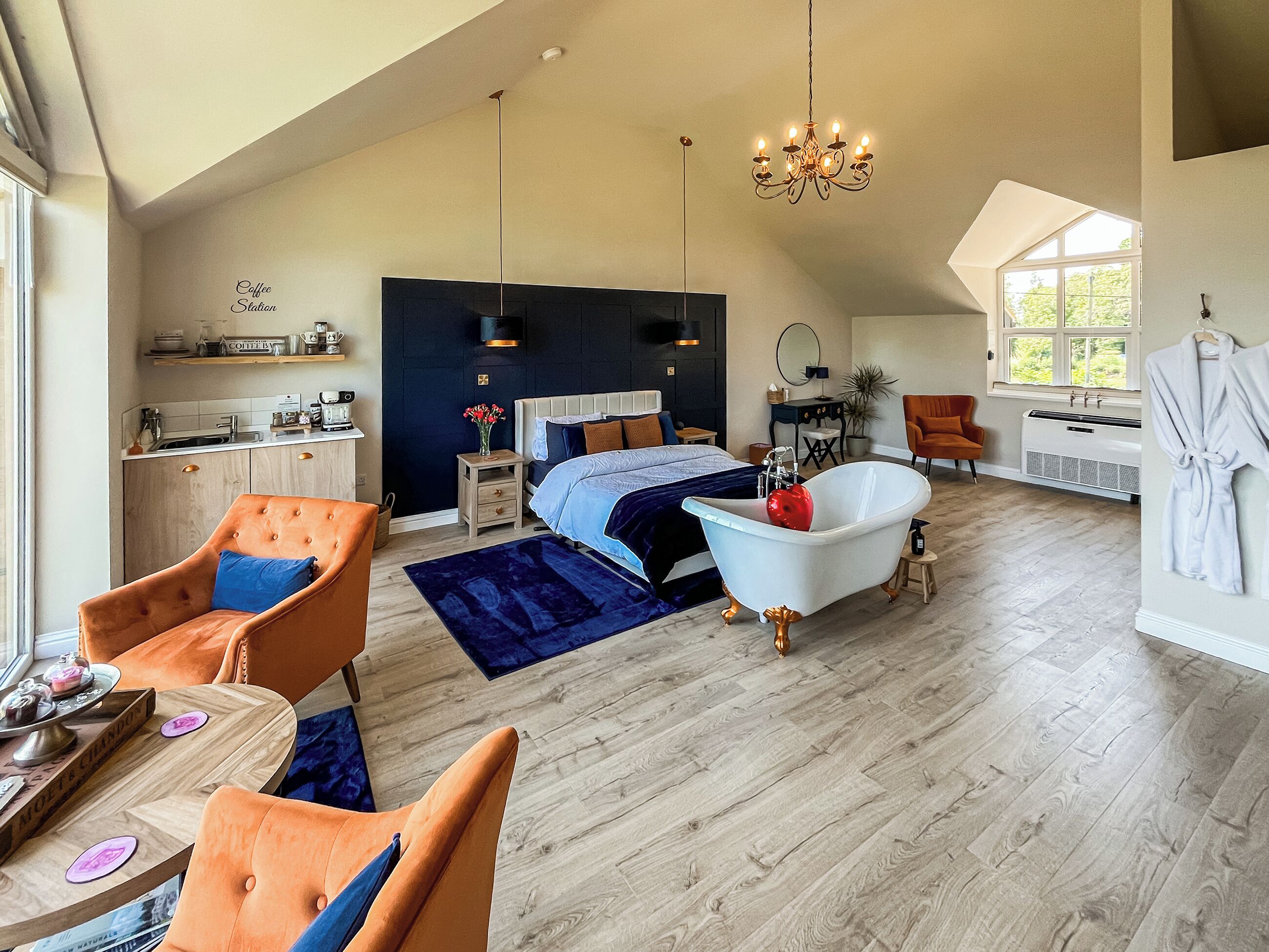 Une pièce spacieuse comprenant un grand lit, un coin salon avec des fauteuils, une table à manger, une baignoire et un coin cuisine.