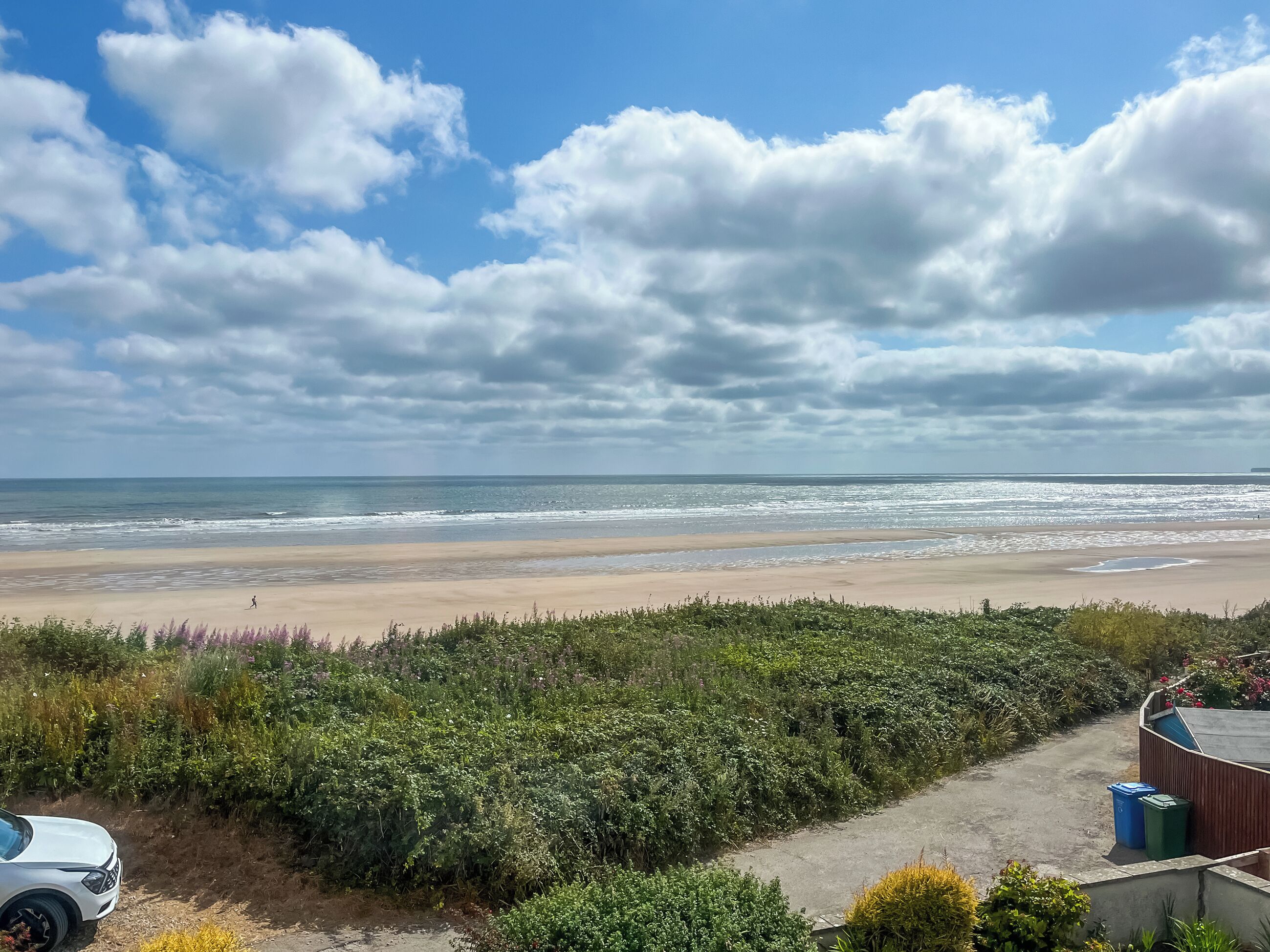 A beach view with a path leading to a building, a parked car, and a clear sky.