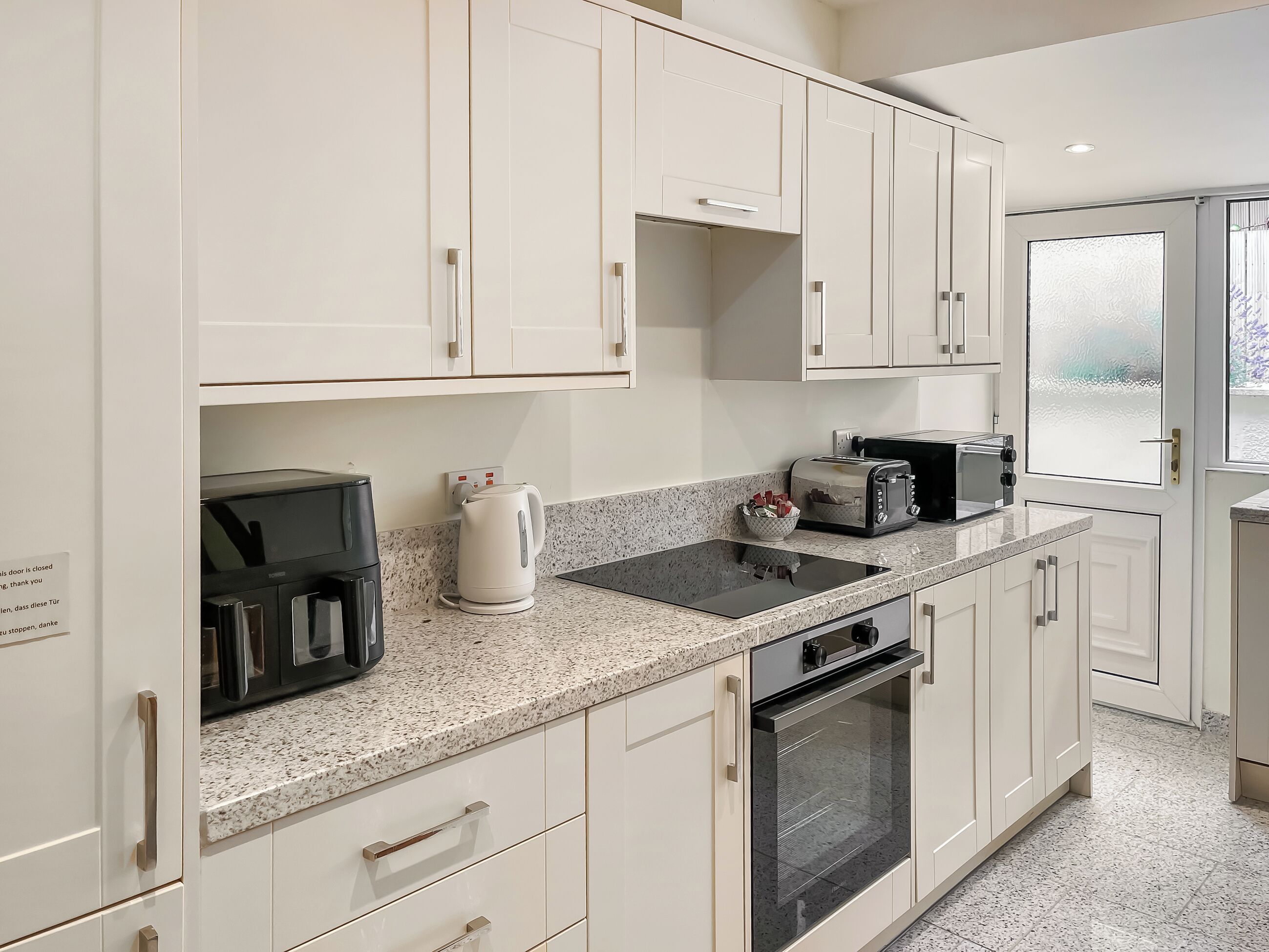 Una cocina moderna con muebles blancos, encimera de granito, cafetera, tostadora y horno.