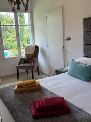 A bedroom with a bed, a chair, a nightstand, a lamp, and a view of the outdoors. - Spacious villa in a quiet location, 5 bedrooms, private pool, near the ocean (Grimaud)