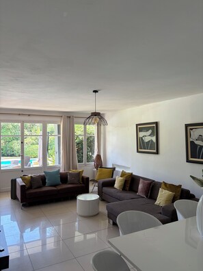 A modern living room with a sofa set, a coffee table, and a dining table. There are large windows providing natural light and a view of the outdoors. - Spacious villa in a quiet location, 5 bedrooms, private pool, near the ocean (Grimaud)