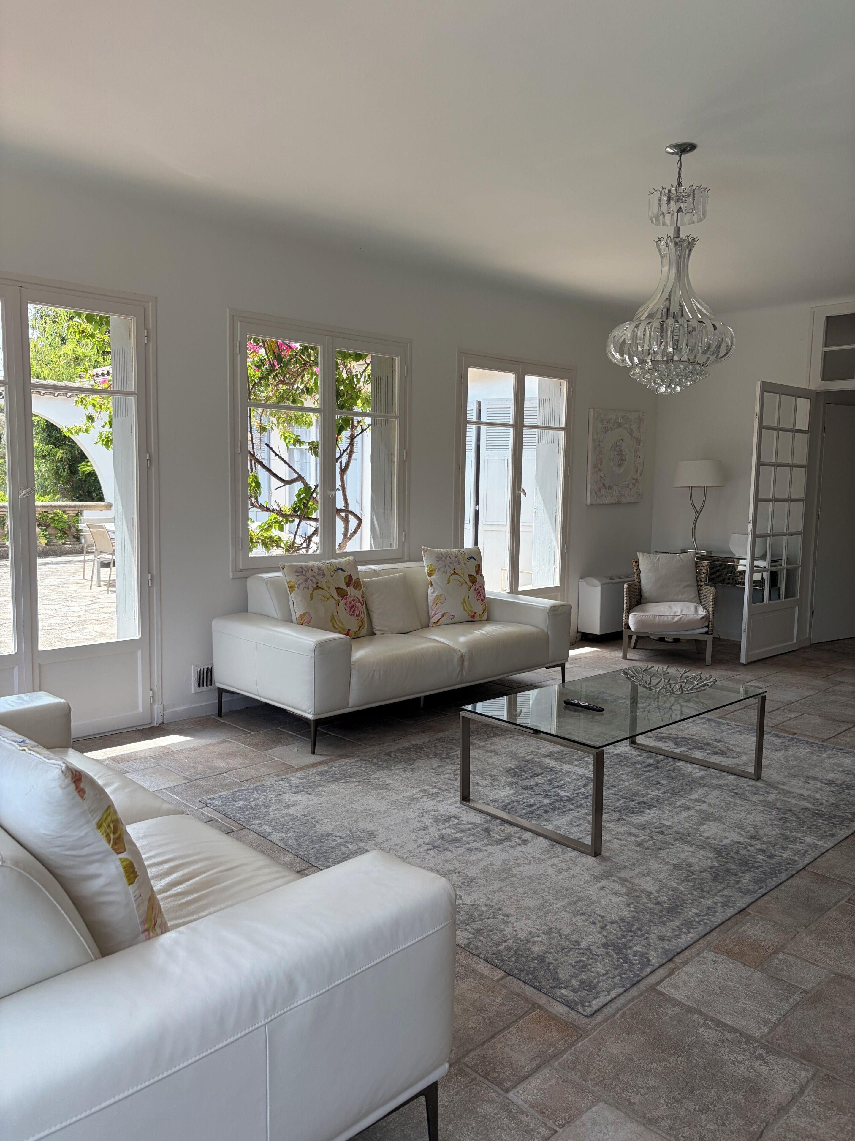 A modern living room with a white sofa, a glass coffee table, and a chandelier.