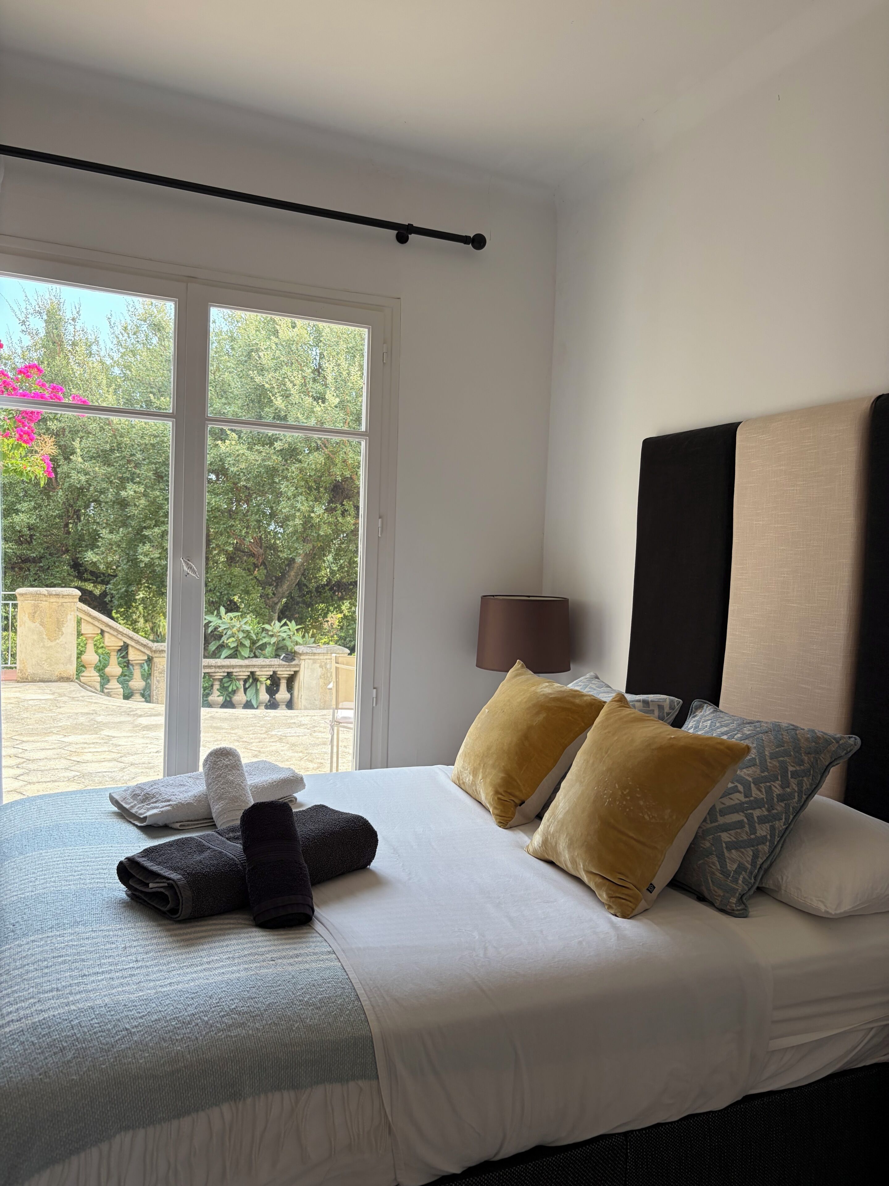 A hotel room with a bed, pillows, a bedside lamp, and a view of the outdoors.