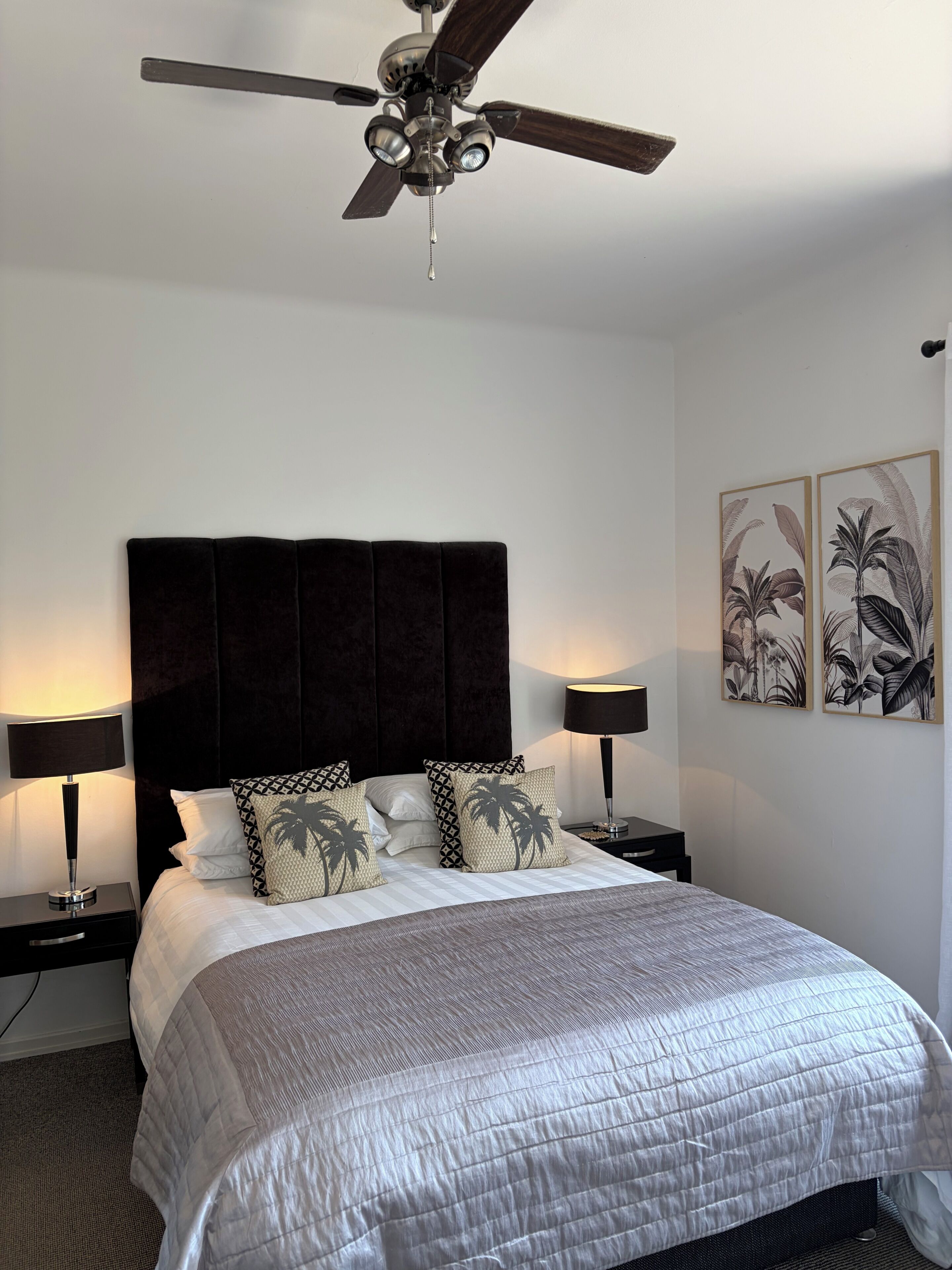 Een hotelkamer met een bed, twee bedlampen, een plafondventilator en kunst aan de muur.