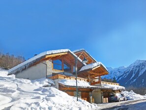 Eine Holzhütte mit geneigtem, schneebedecktem Dach, vor einer Bergkulisse gelegen.