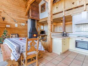 Accogliente interno di una baita in legno con camino, mobili in legno, un tavolo da pranzo con un albero di Natale e un angolo cottura.