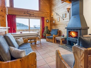 Un intérieur de chalet chaleureux avec une cheminée, des meubles en bois et une vue magnifique à travers de grandes fenêtres.
