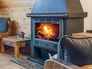 Un poêle à bois muni d’une grille en métal, un banc en bois et une chaise dans une pièce aux murs en bois.