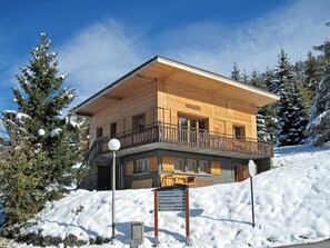 Eine Holzchalet mit Balkon, umgeben von schneebedeckten Bäumen.