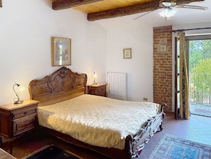 Une chambre avec un lit en bois, des lampes de chevet, un radiateur et une vue sur un espace extérieur, visible à travers une porte vitrée.