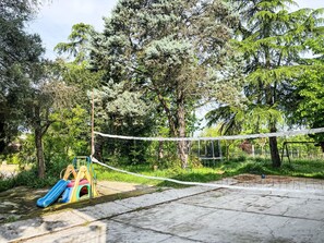 Une aire de jeux avec un toboggan et une structure d’escalade, entourée d’arbres et délimitée par une barrière en corde.