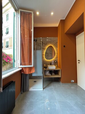 A modern bathroom with a glass shower enclosure, a vanity with a marble countertop, and a view of a building outside. - SAN VINCENZO MODERN APARTMENT (Genova)