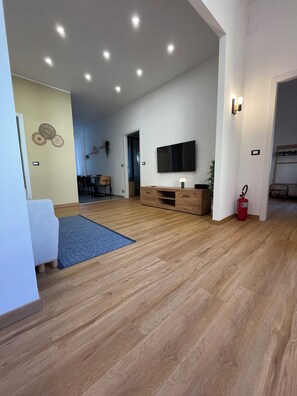 A spacious living area with a wooden floor, a flat-screen TV mounted on the wall, and a blue rug. - SAN VINCENZO MODERN APARTMENT (Genova)