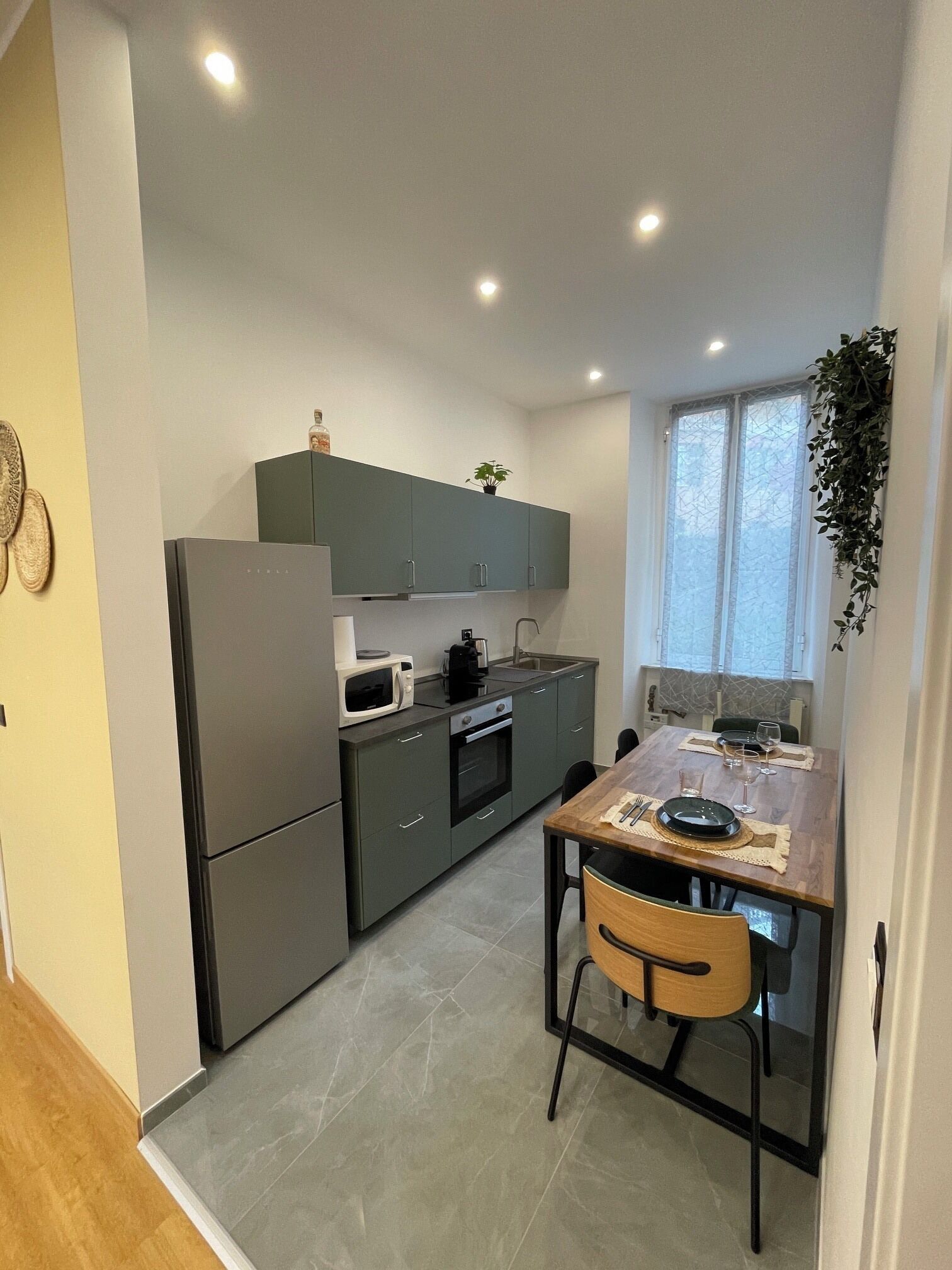 A compact kitchen with a refrigerator, microwave, and stove. There is a dining table with chairs and a window with a view.