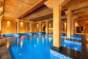 Una piscina interior con columnas de piedra y bordes con azulejos azules.