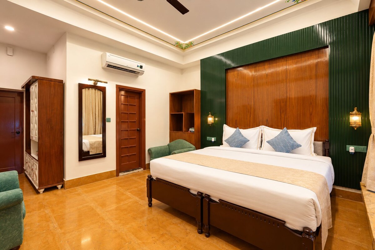 Una habitación de hotel con una cama grande, un armario, un espejo, un equipo de aire acondicionado y una pared verde decorativa.