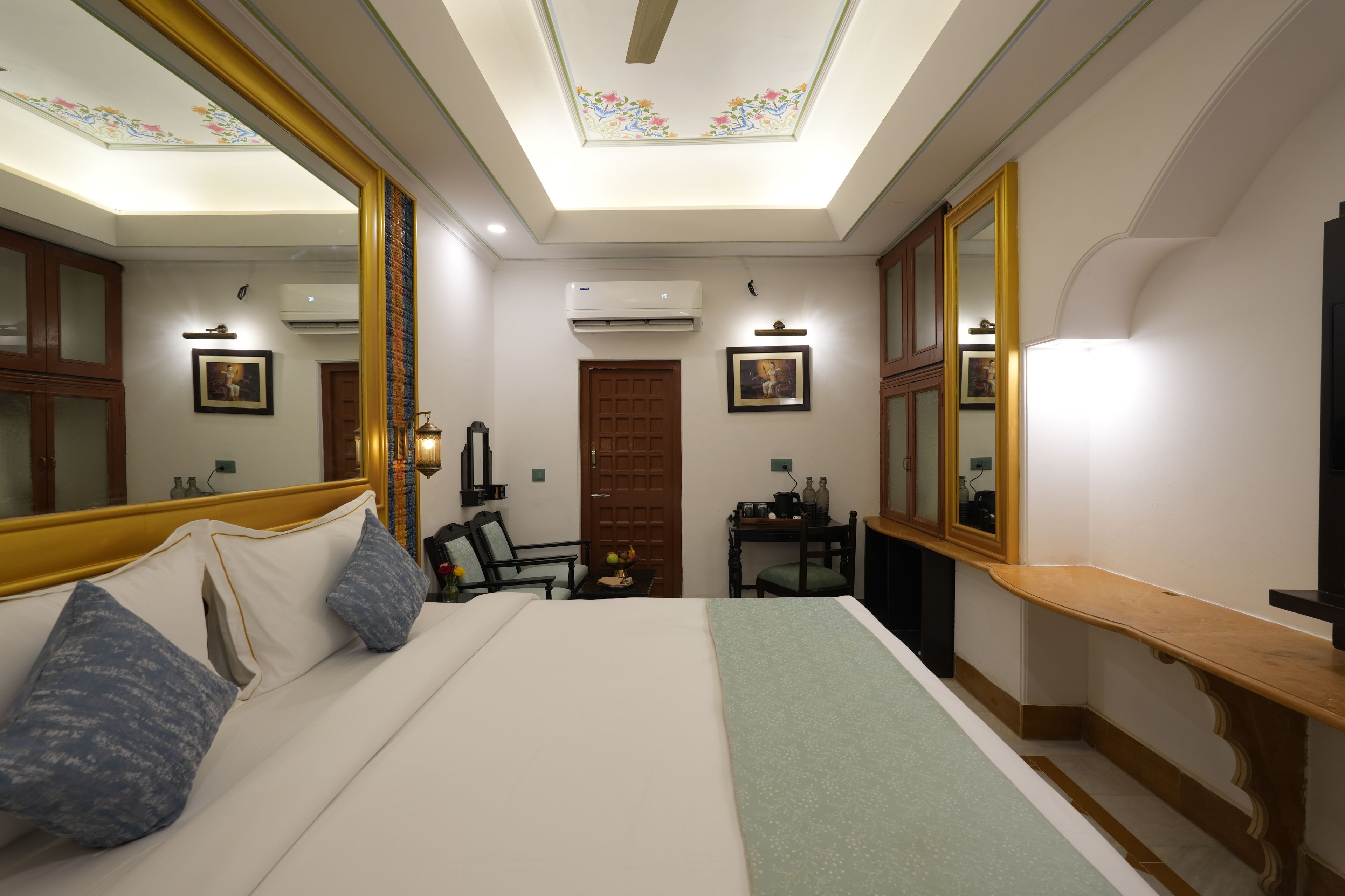 Ein Hotelzimmer mit einem großen Bett, einem Schreibtisch, einem Sessel, einem Spiegel und einer Decke mit Verzierungen.