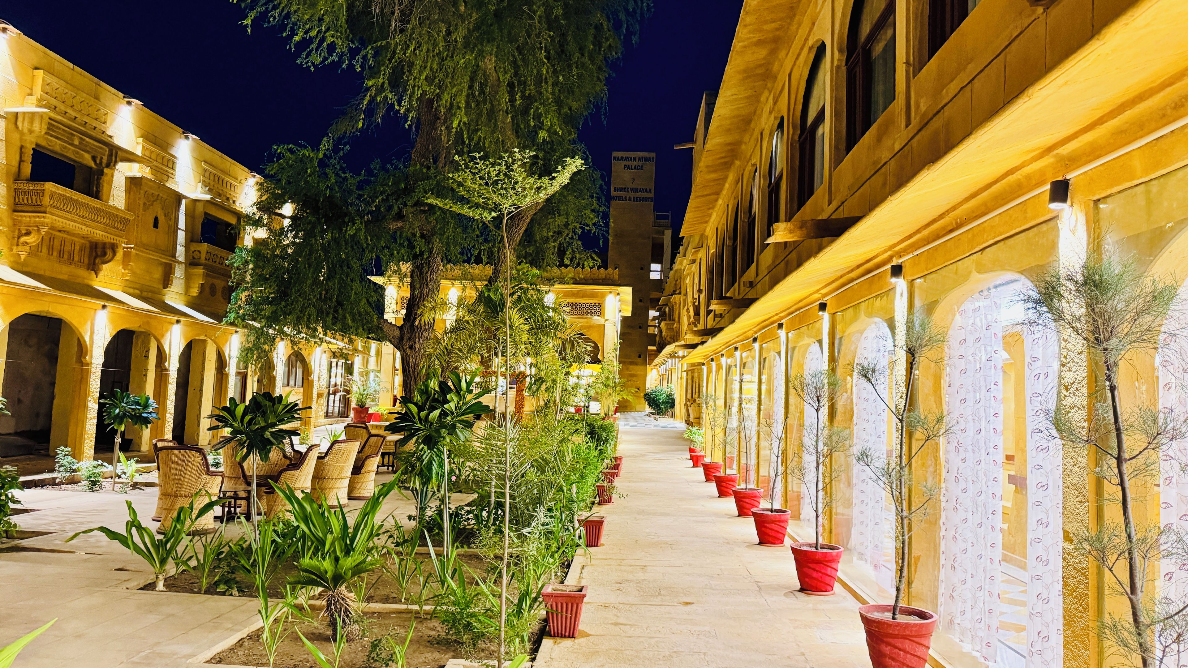 Un patio con un sendero central flanqueado por plantas en macetas y columnas, que conduce a un edificio con un letrero que indica un hotel y resort.