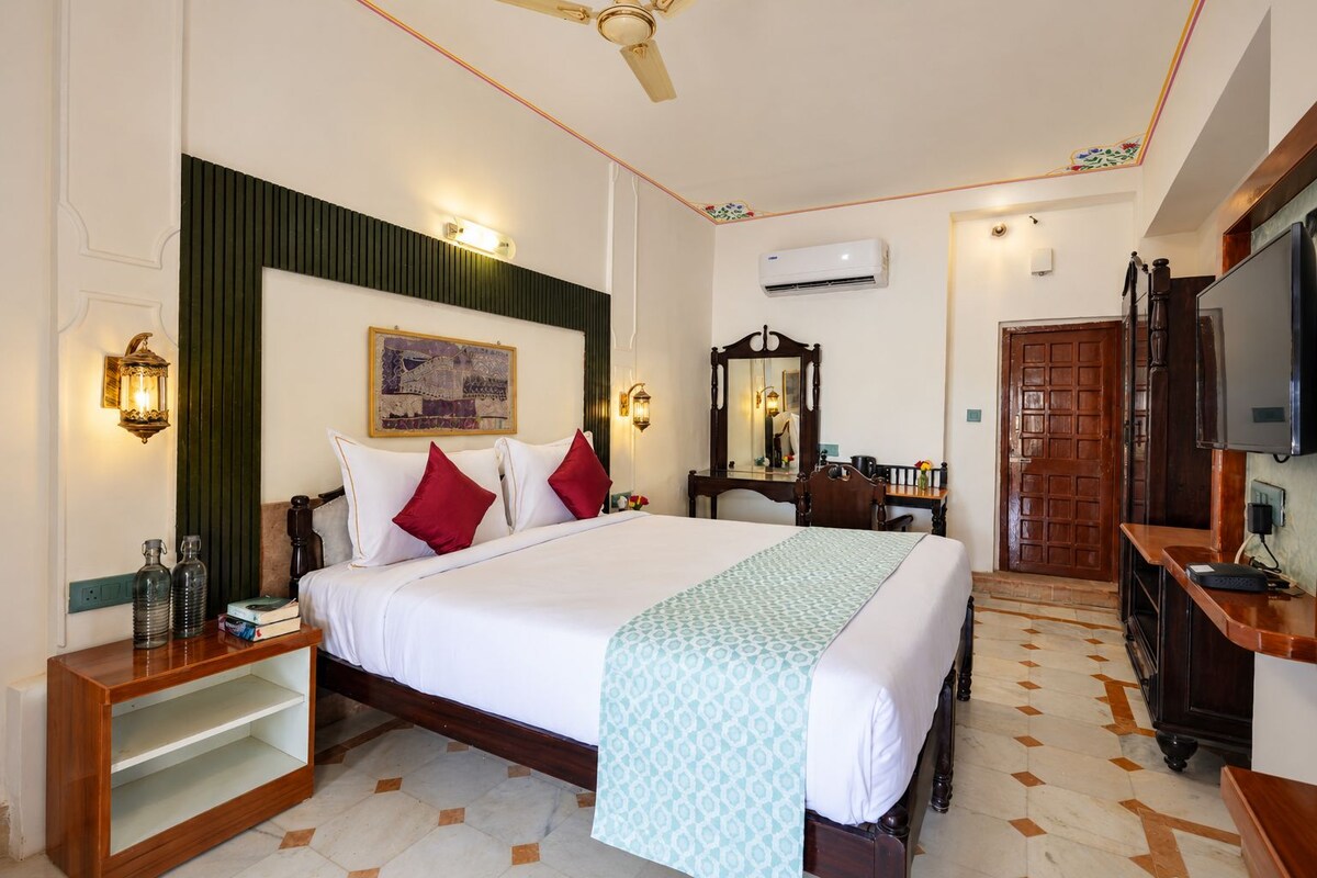 Habitación de hotel con cama, mesita de noche, lámpara, aire acondicionado, armario y televisor.