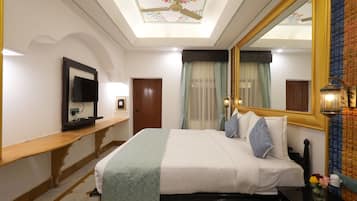 A hotel room with a bed, a bedside table, a mirror, a ceiling fan, and a window with curtains.