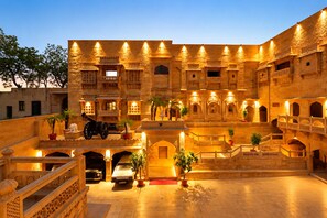 Un edificio histórico con varios niveles, arquitectura ornamentada y un patio con un automóvil y un cañón.