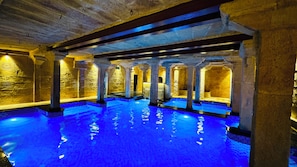 Una piscina interior con paredes y columnas de piedra, iluminada por una luz cálida.