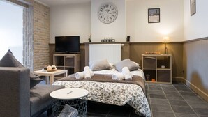 Une chambre d’hôtel avec un lit, une télévision, une horloge et une petite table avec une lampe.
