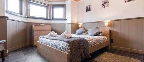 A bedroom with a bed, bedside lamps, a dresser, and a window.