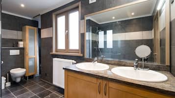 A modern bathroom with two sinks, a large mirror, and a toilet.