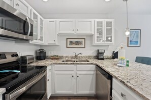 A modern kitchen with white cabinetry, a stainless steel range, a built-in microwave, a coffee maker, and a sink. - Crystal Beach Condo | Walk to the Gulf (Destin)