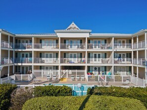 Een hotel met meerdere verdiepingen, balkons, een zwembad en een helderblauwe lucht.