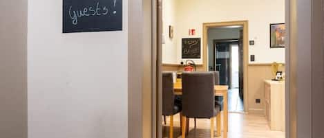 A hotel entrance with a welcome sign, a number '2' above the door, a doormat with a message, and a view into a dining area with a table and chairs.
