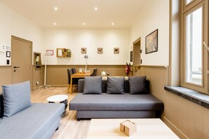 Een hotelkamer met een bank, een kleine tafel, een eethoek met tafel en stoelen, en een raam met uitzicht.