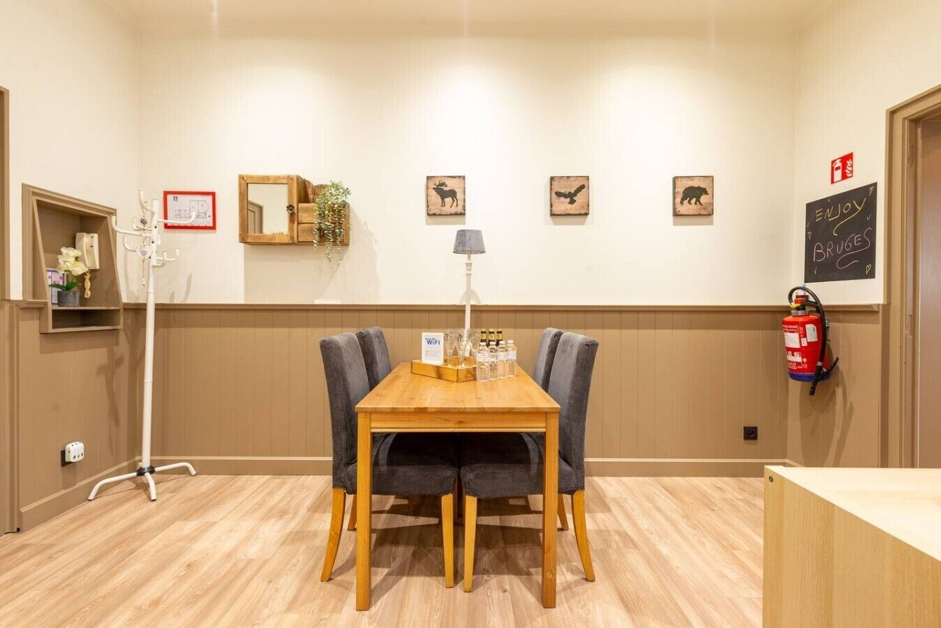A hotel room with a wooden table, two chairs, a lamp, and a fire extinguisher on the wall.