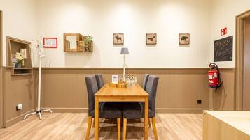 A hotel room with a wooden table, two chairs, a lamp, and a fire extinguisher on the wall.