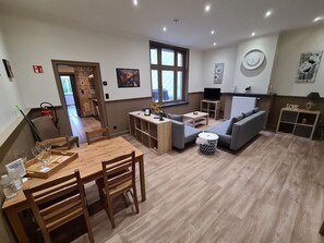 Een ruime woonruimte met een houten eettafel, banken en een televisie.