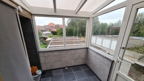 Un petit balcon fermé offrant une vue sur un jardin et des immeubles.