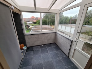 Een klein, afgesloten balkon met uitzicht op een tuin en gebouwen.