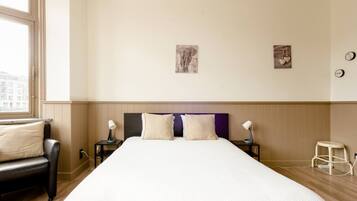 A hotel room with a large bed, two bedside tables, a chair, and a window.