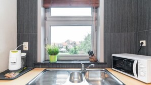 A kitchen with a stainless steel sink, a microwave, a potted plant, and a window with blinds. - Enjoy Bruges Charming Damse Vaart View Apartment (Brugge, Vlaanderen, BE)