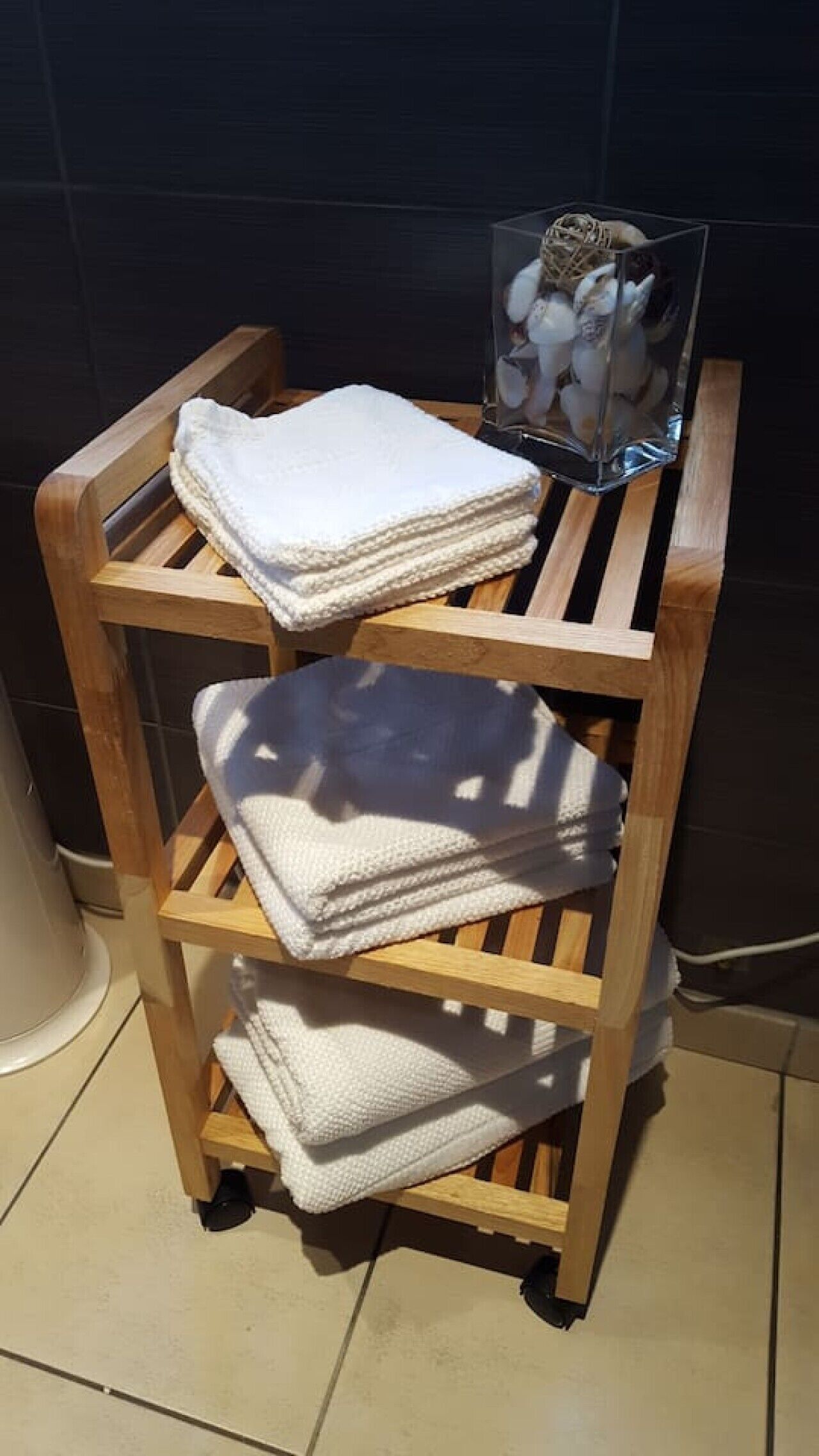 Une étagère en bois avec des serviettes pliées et un récipient en verre contenant des objets décoratifs.