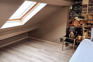 Een kamer met een schuine kap, dakraam en uitzicht op een stadsbeeld.