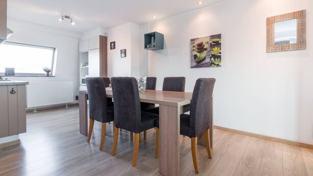 Un moderno comedor con una mesa y sillas de madera, una cocina al fondo y una ventana con vistas.