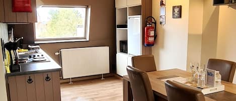 A compact kitchen with a stove, sink, and cabinets, a dining table with chairs, and a fire extinguisher on the wall.