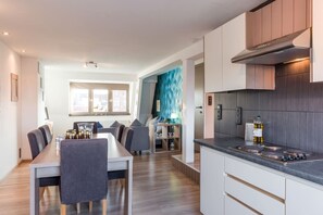 Een moderne keuken met een eethoek, houten vloeren en uitzicht door een open deur.