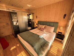 Ein Schlafzimmer mit Holzwänden, einem Bett, einem Nachttisch, einer Wandlampe und einer Tür zu einem Badezimmer.